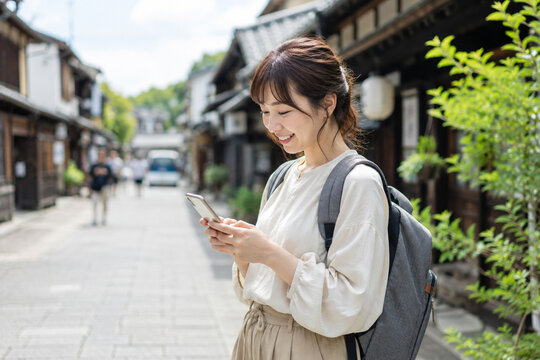 古い町並みでスマートフォンを見る笑顔の女性