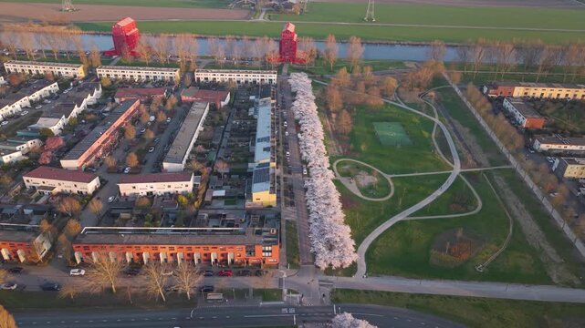 Aerial view of the colorful Regenboogbuurt residential neighborhood featuring modern houses, a canal, and blooming cherry blossom trees in Almere, Flevoland, Netherlands.