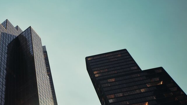 Tall buildings rise against a clear blue sky. The sunlight reflects off glass surfaces. This scene captures the architecture of the city during the day.