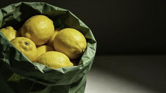 Fresh yellow lemons arranged inside green paper grocery bag