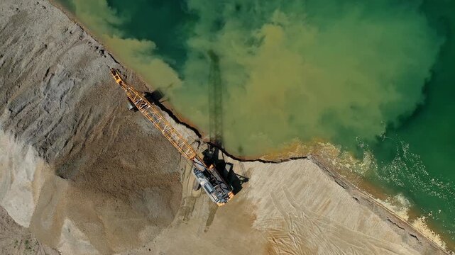 Aerial view of crawler crane dredging sand and gravel from lake in open pit mine.