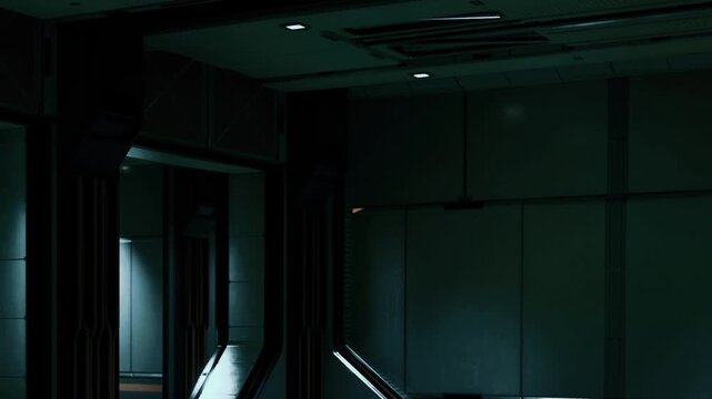 In a modern and dimly lit indoor space, shadows cast by walls create shapes around a corridor. Soft light comes from an open area, hinting at more space beyond.