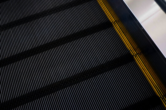 Close-up texture of black escalator steps with yellow safety edge lines in a modern building.