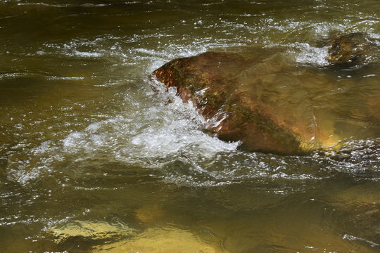 clear flowing stream of shadow water rushing over smooth rocks in a natural outdoor