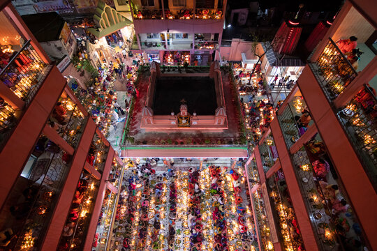 Dhaka, Bangladesh - 09 November 2021: Aerial view of Hindu devotees at the Swamibag Loknath Temple during the Rakher Upobash festival, with rows of glowing oil lamps illuminating the courtyard.