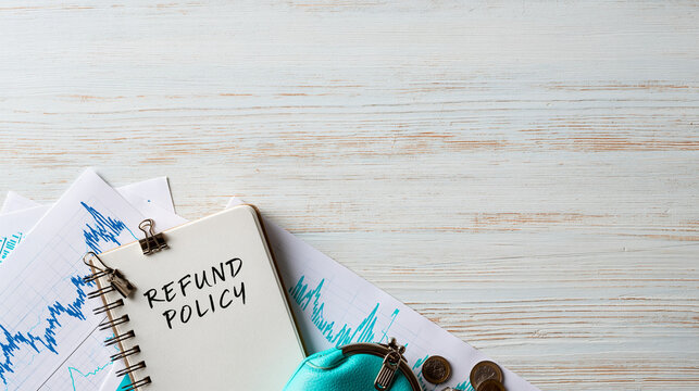 Refund Policy Document: A notebook with REFUND POLICY handwritten, rests on financial charts, accompanied by coins and a coin purse, symbolizing financial management and consumer rights.