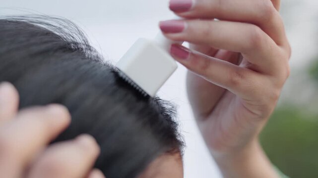Woman applying hair growth serum with scalp massager applicator on hair roots for treatment.