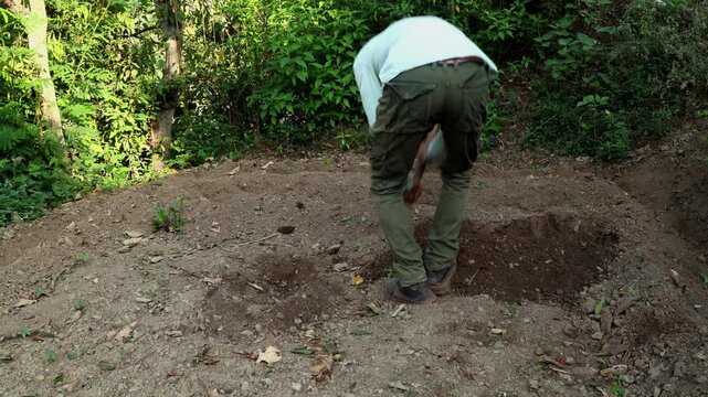 Real-time close-up video of a young farmer manually preparing soil with a traditional hand hoe to create planting furrows for ginger during summer in Himachal Pradesh, India.