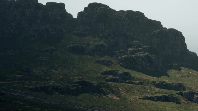 Sunlight shines on rocky landscapes in a mountain area. The time is midday with clear skies. The scene shows natural formations and green vegetation around the rocks.