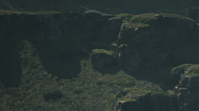 In a remote area, large rock formations rise from green grass. The sun casts shadows on the rocks, highlighting their shapes. This scene shows the natural beauty of the wilderness.