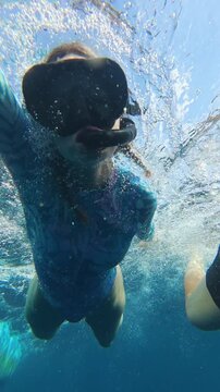 Vertical underwater selfie of two snorkelers in Lovina, Bali, wearing masks while swimming in clear blue ocean water with bubbles and action camera perspective.