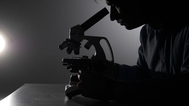 Scientist silhouette peering into a microscope in a dim lab, focused on research and discovery during a detailed biological or medical investigation and experiment