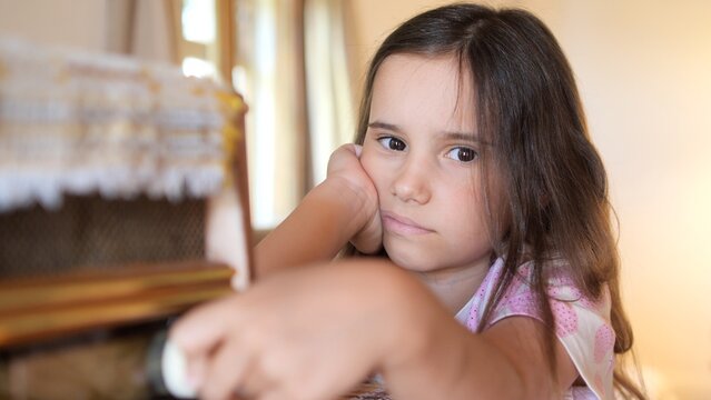 Young girl resting her head on her hand, looking with a sad and apathetic expression, experiencing feelings of boredom and unhappiness while spending time indoors