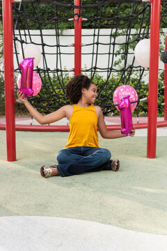 Girl celebrating eleven birthday with number balloons at playground