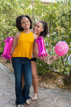 Sisters celebrating birthday holding eleven balloons outdoors