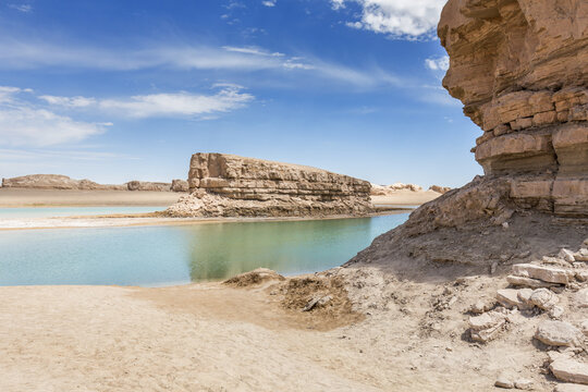 Layered rock formations and water-filled yardang in arid desert under clear blue sky.