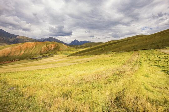 A natural landscape of rolling grasslands, colorful hills, and distant mountains under a cloudy sky.