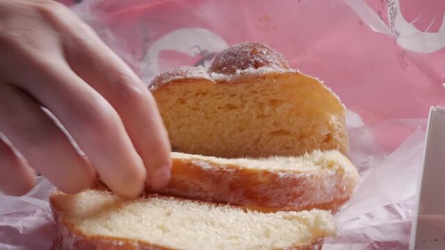 Person takes slices of sweet Mexican bread known as pan de muerto from pink paper on a table.