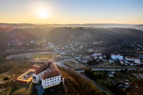 Aerial view of a historic chateau situated on a hill overlooking a small town and rural landscape during golden hour in Czech Republic.