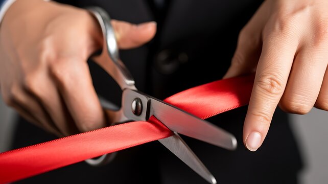 A close-up photograph of two hands performing an official ribbon cutting ceremony with metallic scissors for a new business launch