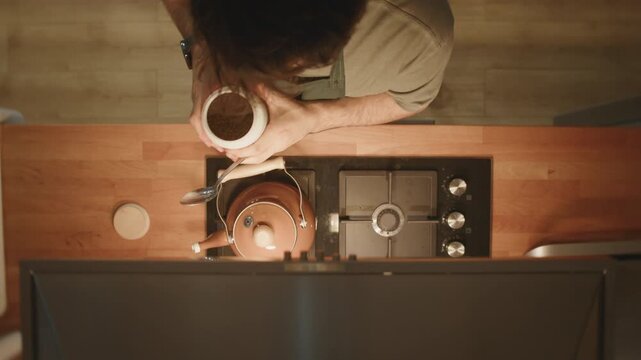 Man measuring loose tea leaves with spoon into copper kettle, top view kitchen scene