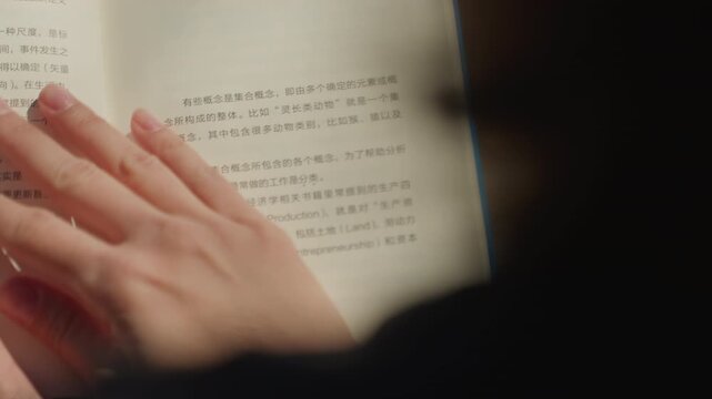 Close up of hands turning pages in book with Chinese text fingers gently touching paper. Soft natural light creates shadows on open spread emphasizing texture details and calm interaction