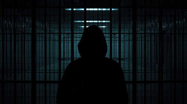 Anonymous individual silhouette behind metal bars creates mysterious prison scene