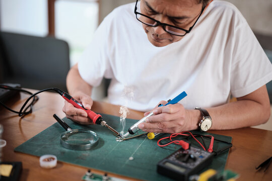 Close-up, man's hand repairs home electrical appliance, disassembling and soldering circuit board, focusing on precision detail, DIY fix tools, electronics component workshop hobby, expert handyman.