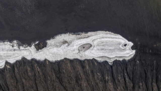 Aerial view of the volcanic landscape of Landmannalaugar featuring contrasting textures of white snow patches against dark volcanic sand and rugged terrain in Hella, Rangarthing ytra, Iceland.