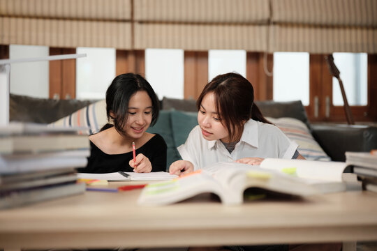 Two Asian teenage girls learning tutorials at home together, reading textbooks, writing notes, self-tutorial exams, preparation for back to school, Homeschooling study, knowledge education lifestyle.