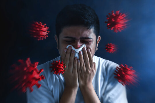 Man sneezing nose with tissue on dark background