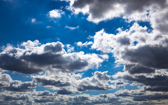 Dramatic sky background with dark and white cumulus clouds under intense bright sunlight