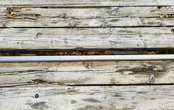 Weathered grey wooden boardwalk planks background with central horizontal metal rail divider
