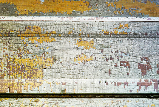 Heavily cracked and peeling white paint texture over weathered yellow wood siding background
