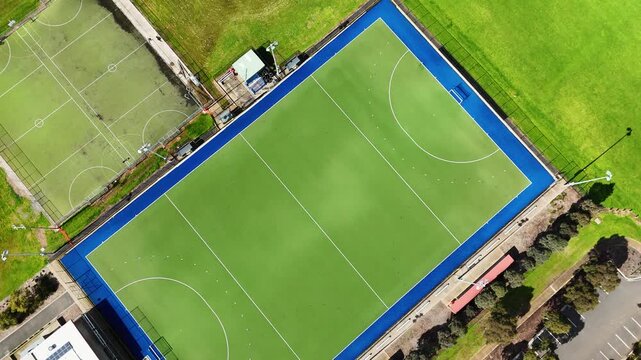 Aerial top-down view of a synthetic turf hockey pitch with blue border lines&nbsp;and a multi-purpose sports ground at a public sports facility in Wyndham Vale, Melbourne, Australia. 