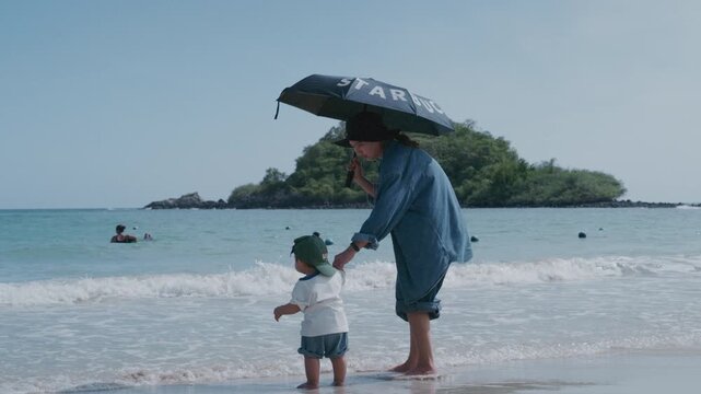 Cute Asian toddler playing with sand on tropical beach during family vacation.