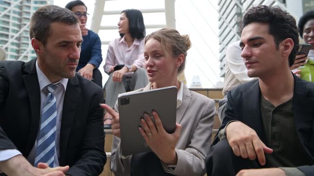 International business professionals from diverse ethnic backgrounds sitting together on city steps, discussing ideas and using digital devices in an urban setting