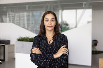 Portrait of serious Arab businesswoman in black blouse standing with arms crossed in contemporary...