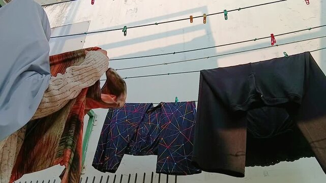 Woman Taking Dry Clothes Off a Clothesline After Air Drying Outdoors