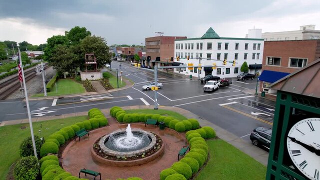 Aerial view of a small town square with a fountain and clock tower on a cloudy day.