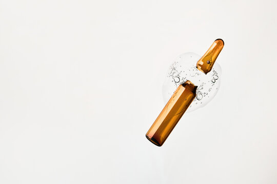 Broken glass ampoule spilling cosmetic serum with air bubbles on white background