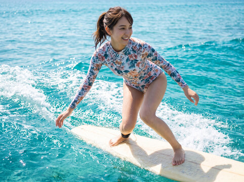 青い海原でボードの上でバランスを取りながら笑顔で波に乗る女性
