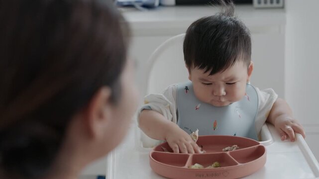 Asian baby boy self feeding sweet corn using baby led weaning method at home.	