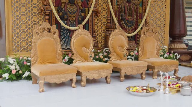 Ornate wedding chairs and ceremonial items arranged on decorated outdoor stage