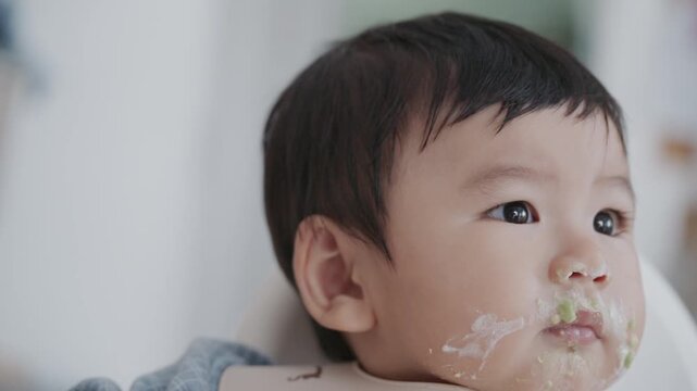 Asian baby boy self feeding sweet corn using baby led weaning method at home.	
