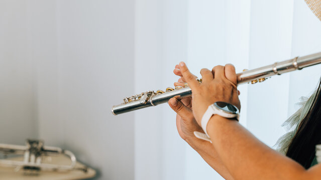 A female flutist in a green shirt sits on a brown couch in her cozy living room, playing a silver flute with concentration