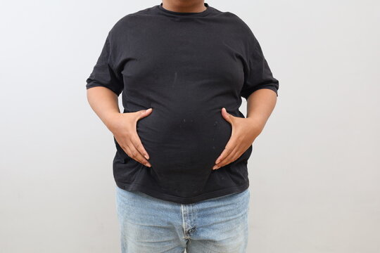 A closeup photo of a man's hand holding his protruding belly, standing isolated against a white background.