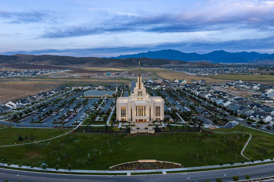 Saratoga Springs, Utah, United States - 22 August 2026: Aerial view of Saratoga Springs Utah Temple glowing during the blue hour, surrounded by lawns, parking lots, and residential neighborhoods.