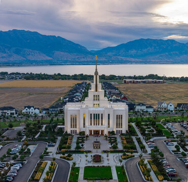 Saratoga Springs, Utah, United States - 22 August 2026: Aerial view of the Saratoga Springs Utah Temple glowing during the blue hour with surrounding gardens and distant mountains.