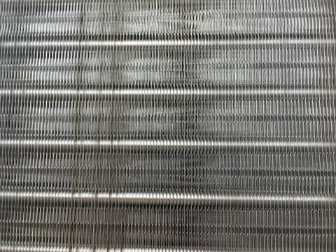 Metal condenser coils texture background close up. Industrial aluminum cooling fins macro background. Metallic heat exchanger grill abstract pattern.